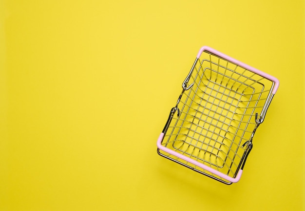 Un panier d'achat en miniature vide sur un fond jaune représente le concept de shopping.