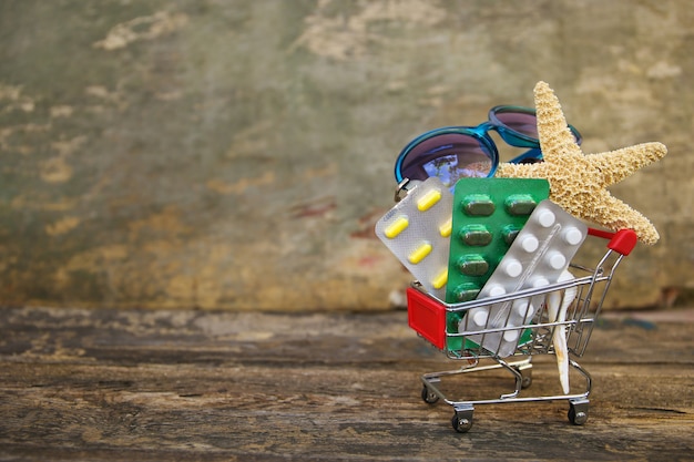 Panier d'achat avec des pilules, des lunettes de soleil, des coquillages sur une vieille surface en bois