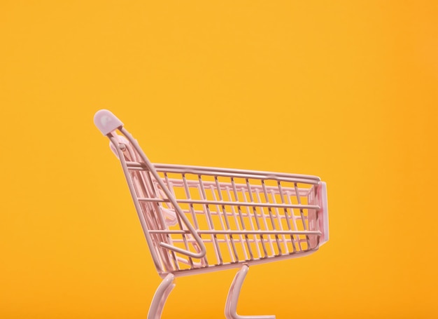 Le panier d'achat rose vide se dresse sur un fond jaune vif Concept de remise de vente et de shopaholisme