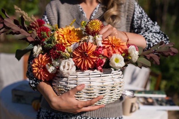 Un panier blanc en osier avec des dahlias et des asters de fleurs d'automne de saison dans ses mains