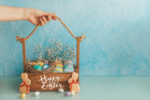 Panier en bois avec des oeufs de Pâques et des bonbons sur la table Une salle de cuisine ordinaire avec des fleurs dans un concept de Pâques pot