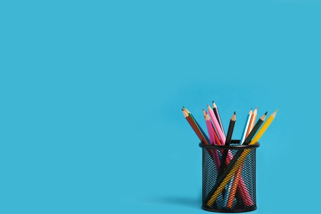 Panier de bureau avec des crayons de couleur sur fond bleu.