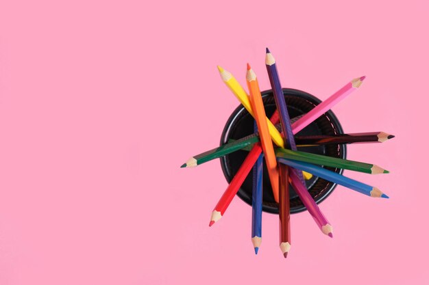 Panier de bureau avec des crayons de couleur sur fond rose.