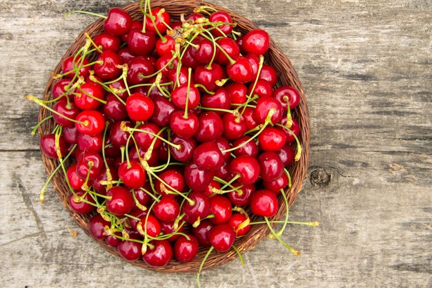 Panier avec des cerises rouges sur une table en bois vintage. Concept de saison des fruits d'été. Vue de dessus