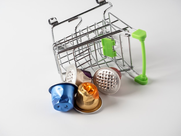 Un panier d'épicerie est placé sur un fond blanc. Des capsules de café en aluminium usagées s'en sont déversées.