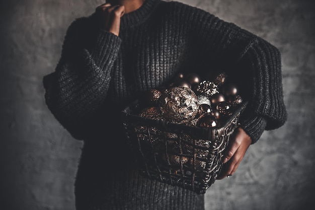 Photo panier en fil plein de jouets de décoration vintage dorés pour arbres de noël ou du nouvel an dans les mains d'une dame dans un pull gris chaud, mise au point sélective, culture carrée