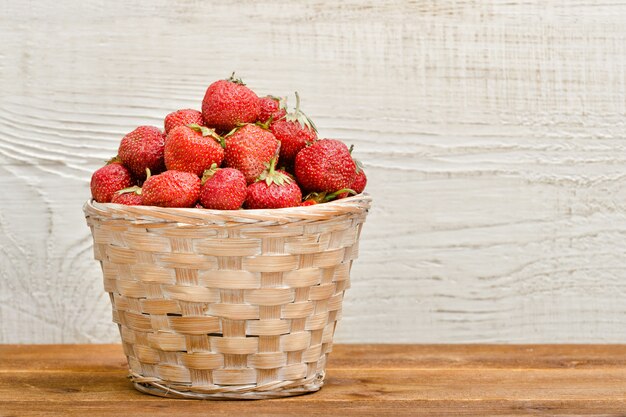 Panier de fraises mûres sur un bois blanc.