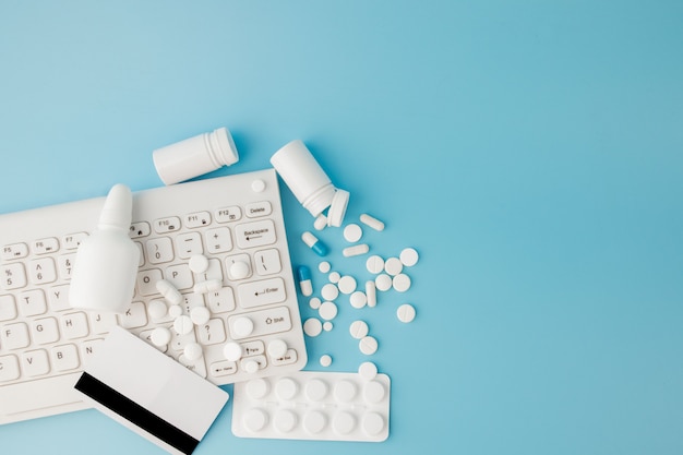 Panier jouet avec médicaments et clavier. Pilules, plaquettes thermoformées, bouteilles médicales, thermomètre, masque de protection sur fond bleu. Vue de dessus avec place pour votre texte