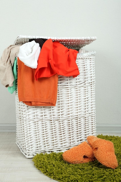 Panier à linge plein sur tapis de couleur sur fond de mur gris