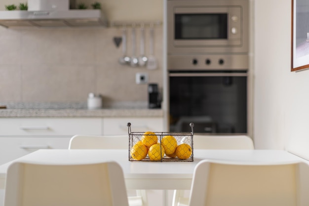 Panier en métal avec des citrons jaunes mûrs sur une table à manger blanche arrière-plan flou de meubles de cuisine