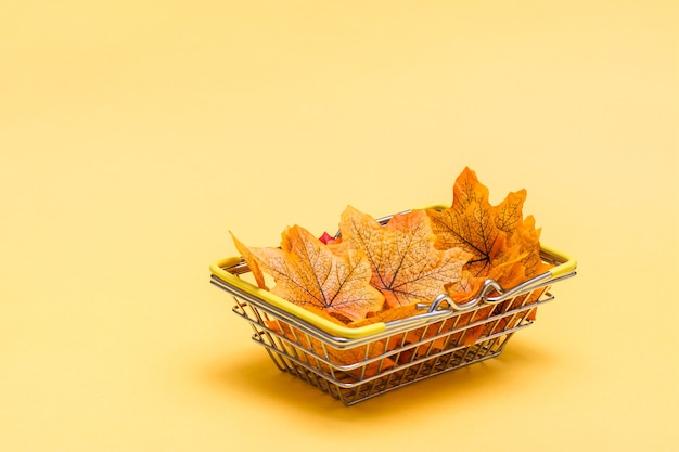 Un panier en métal dans un magasin rempli de feuilles d'automne sur fond jaune. Ventes de cadeaux du Black Friday