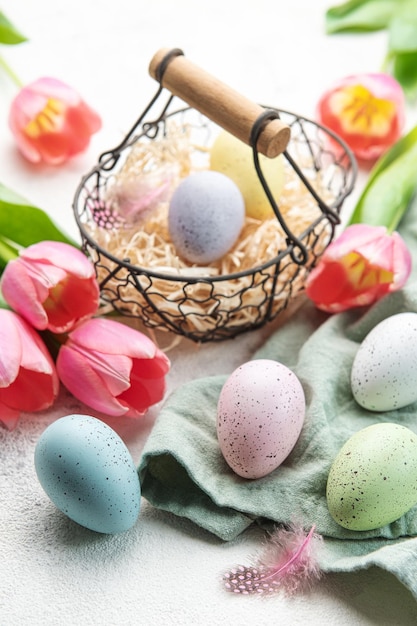 Panier avec des oeufs de Pâques peints en couleurs pastel et des tulipes roses sur un fond de béton