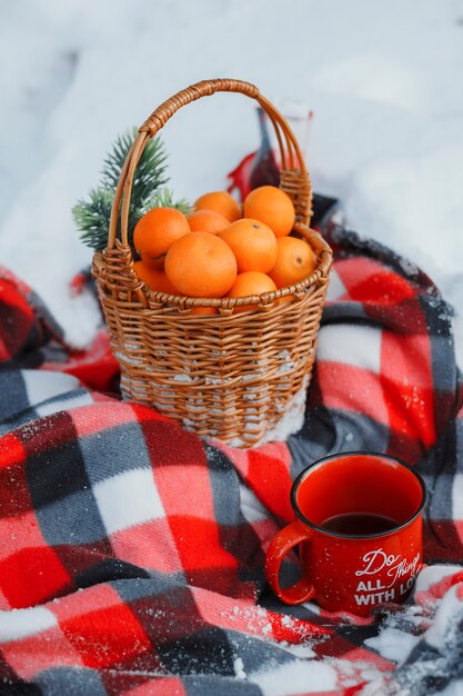 Un panier d'oranges dans la neige, une tasse de thé et une couverture rouge