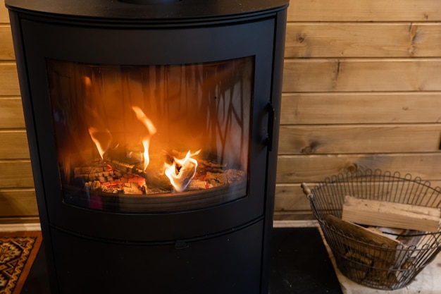 Panier en osier avec bois de chauffage près de la cheminée d'incendie Poêle à bois avec corps en métal et porte vitrée dans une maison confortable avec un intérieur confortable dans la chambre