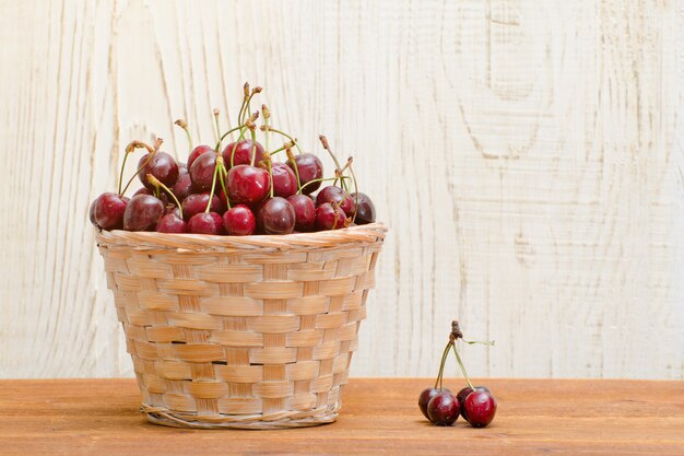 Panier en osier avec des cerises sur une table en bois, espace vide