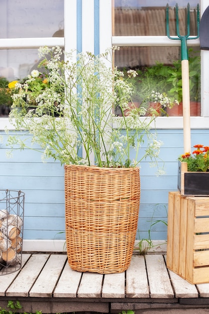 panier en osier avec des fleurs à côté des outils de jardin contre le mur de la maison de campagne décor d'été confortable véranda maison