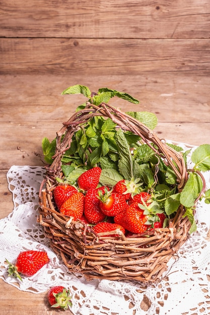 Panier en osier de fraises mûres. Baies fraîches, menthe aromatique. Vieille table en bois, serviette au crochet vintage, style rustique, espace copie