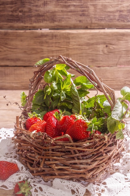 Panier en osier de fraises mûres. Baies fraîches, menthe aromatique. Vieille table en bois, serviette au crochet vintage, style rustique, espace copie