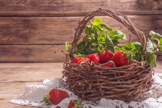 Panier en osier de fraises mûres. Baies fraîches, menthe aromatique. Vieille table en bois, serviette au crochet vintage, style rustique, espace copie