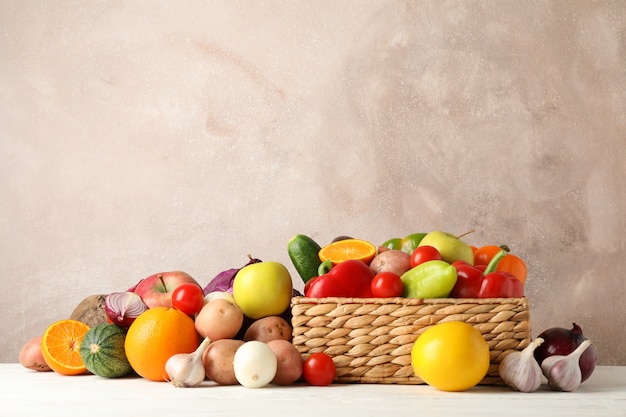 Panier en osier, légumes et fruits sur un espace en bois blanc pour le texte