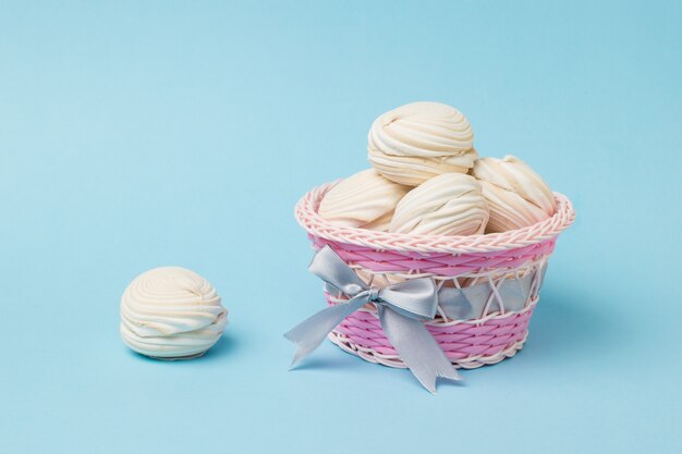 Panier en osier avec meringue à la vanille sur une surface bleue