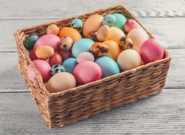Panier en osier avec des oeufs de Pâques colorés sur table en bois
