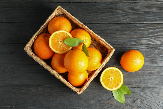 Panier en osier avec des oranges mûres sur table en bois.