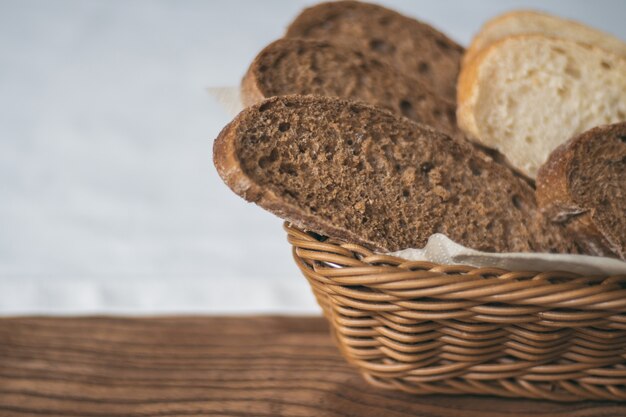 Panier en osier partiellement flou avec du pain noir et blanc sur une nappe blanche, sur une table en bois