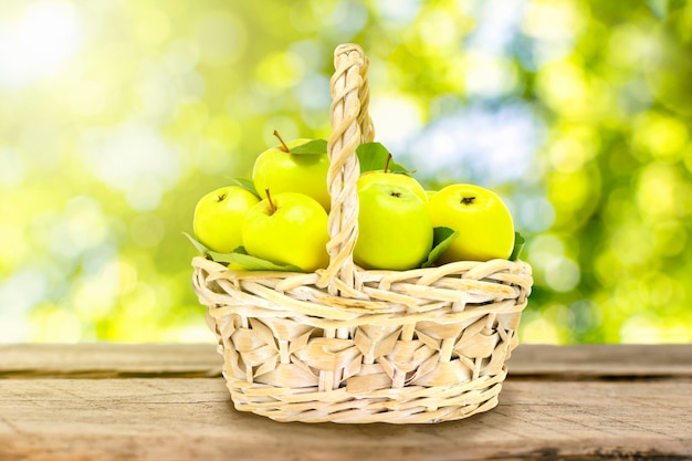 Panier en osier avec des pommes vertes mûres sur une table en bois sur fond de feuilles d'arbres.