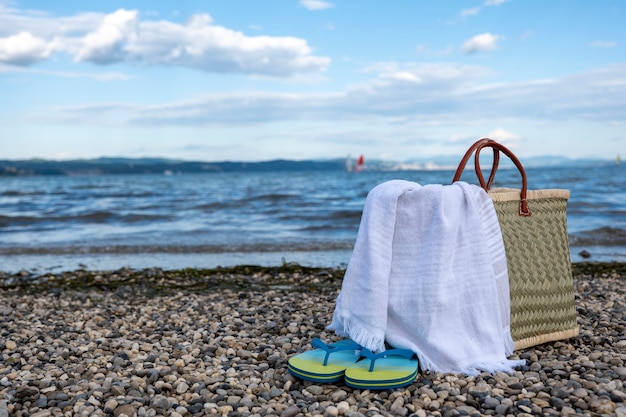 Panier en osier, serviette et chaussons sur une plage rocheuse contre un beau ciel