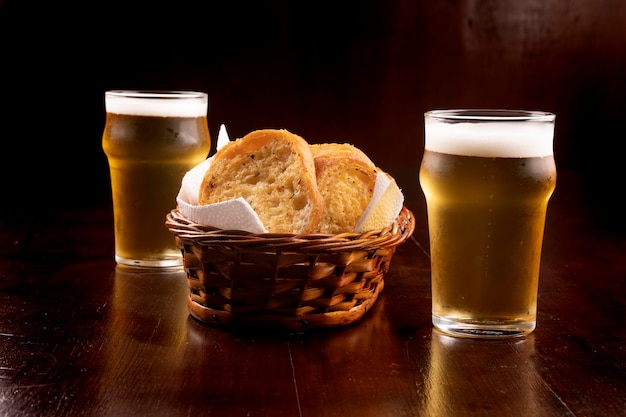 Panier de pain grillé à l'ail et deux verres de bière légère sur table en bois