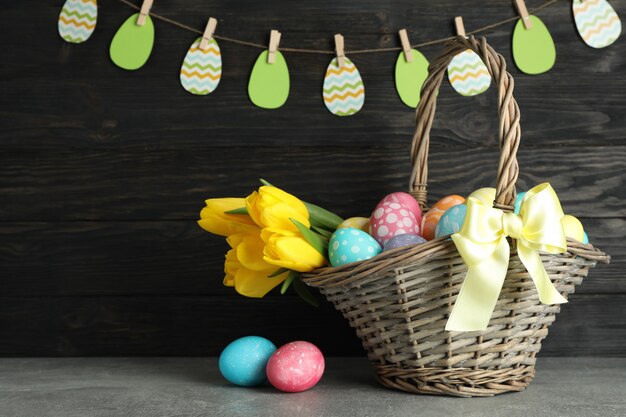 Panier de Pâques rempli d'oeufs colorés et de fleurs sur un fond en bois