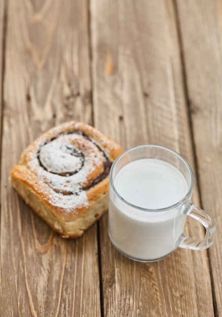 Panier de petits pains faits maison avec de la confiture, servi sur une vieille table en bois avec une tasse de lait