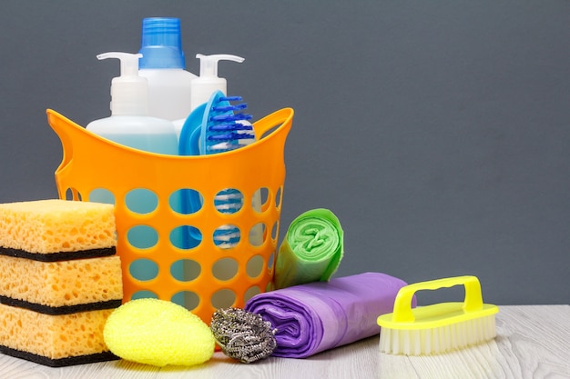 Panier en plastique avec bouteilles de liquide vaisselle, nettoyant pour carrelage, détergent pour fours à micro-ondes et cuisinières. Éponges, sacs poubelles et brosse sur fond gris. Concept de lavage et de nettoyage.