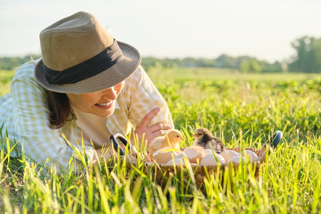 Panier avec des poulets nouveau-nés, femme heureuse au chapeau à la recherche de poussins