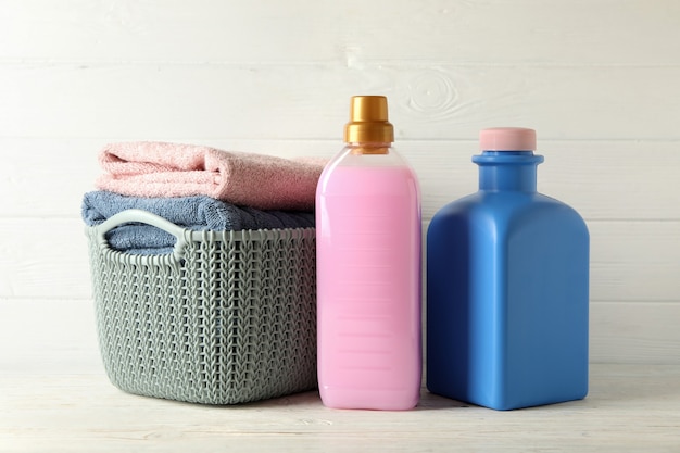 Panier avec des serviettes et des bouteilles avec du liquide de lessive sur une table en bois blanc