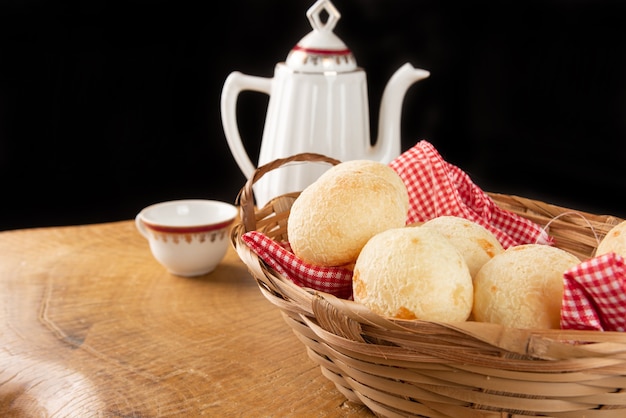 Panier en tissu à carreaux avec pains au fromage sur une surface en bois rustique avec théière et tasse de café