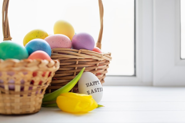 Photo paniers en osier avec des oeufs aux couleurs vives et avec texte joyeuses pâques et fleur