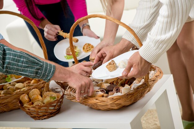 Paniers tissés en gros plan remplis de produits de boulangerie auxquels un tas de mains tendent la main pour prendre la délicieuse pâtisserie.