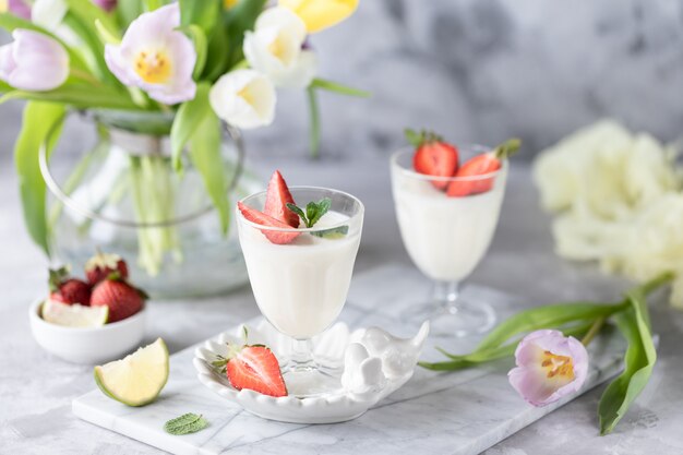 Panna cotta dans des verres en verre avec des fraises sur fond clair. Bouquet de tulipes sur un tableau blanc.