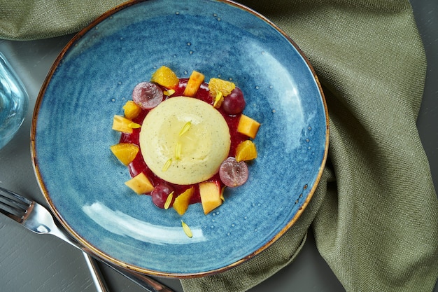 Panna Cotta - un délicieux et beau dessert à base de crème et de vanille avec des raisins et de la pêche dans un bol bleu sur une table en bois. Vue de dessus, mise à plat, espace copie