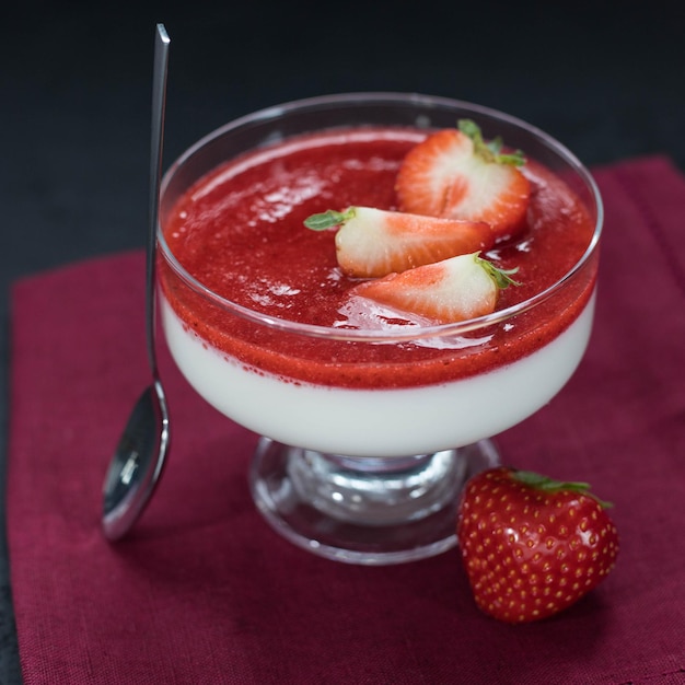 Panna cotta avec sauce aux fraises et baies de fraises dans un bol sur fond noir