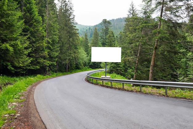 Panneau d'affichage horizontal blanc vide sur le bord de la route Une route incurvée entre la forêt