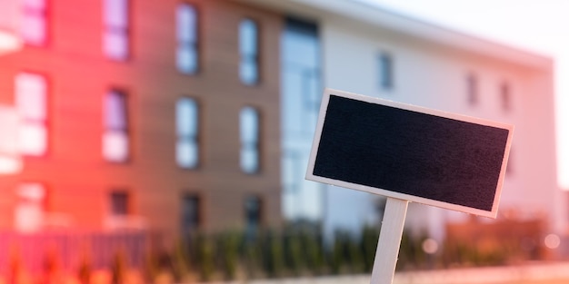 Photo panneau d'affichage noir vierge contre un nouvel immeuble d'appartements modèle de maquette vide panneau d'étiquette maison