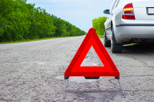 Panneau d'arrêt d'urgence rouge et voiture d'argent cassée sur la route