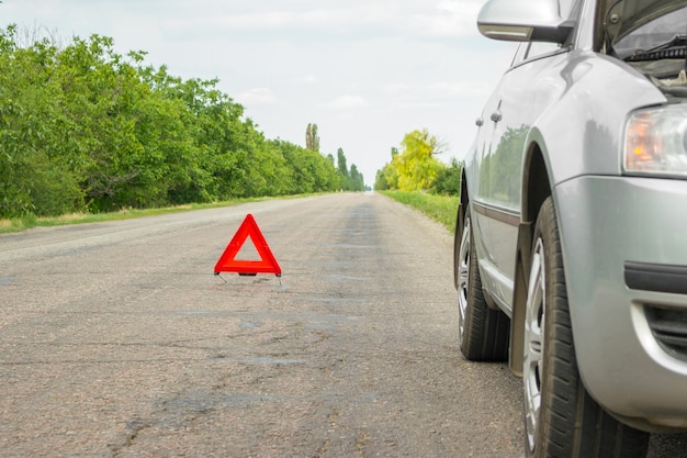 Panneau d'arrêt d'urgence rouge et voiture argent cassée sur la route