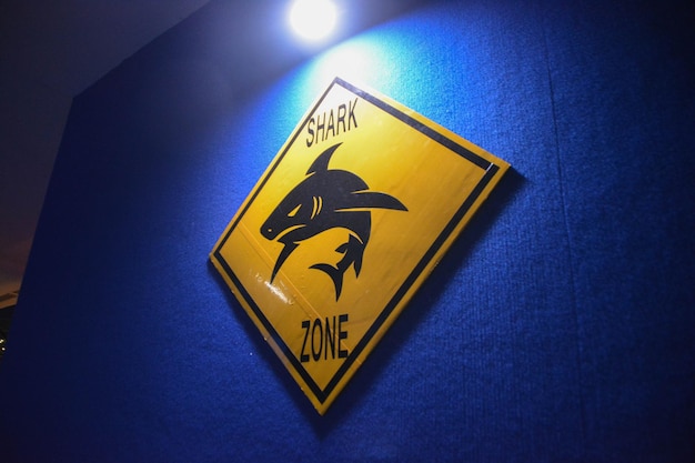 Panneau d'avertissement de requin jaune sur le mur bleu avec lumière brillante