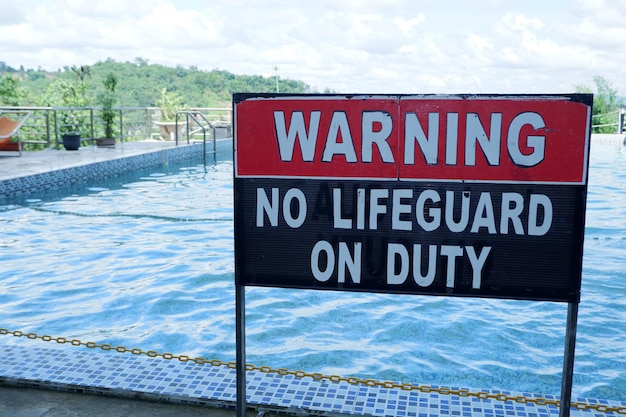 un panneau d'avertissement sans sauveteur en service avec une piscine en décalage à l'arrière-plan