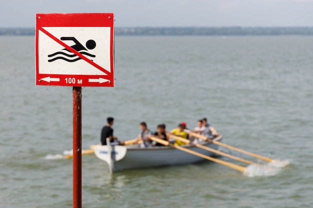 Panneau interdisant la baignade dans cet endroit et bateau à rames en bois avec des gens