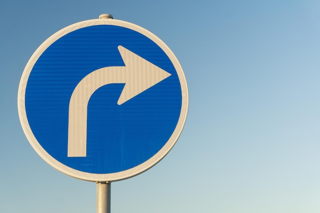 Le panneau de signalisation bleu tournant à droite sur fond de ciel en gros plan